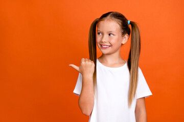 Photo portrait of charming little girl point look interested empty space dressed stylish white clothes isolated on orange color background