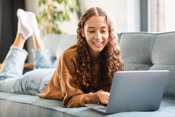 Happy modern adolescent girl enjoys e-learning with laptop at home