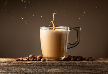 Glass cup of coffee drink, latte or mocha with splashes on a brown background.