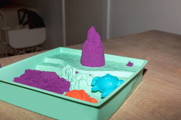 A wooden table with purple kinetic sand and a pink castle on top