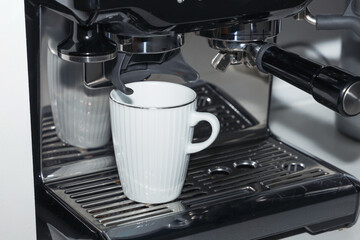 A white coffee cup pouring coffee into a coffee maker.