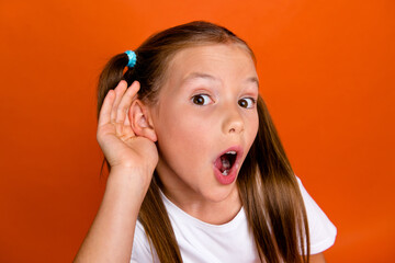 Photo of speechless impressed girl open mouth stare hand near ear eavesdrop isolated on orange color background