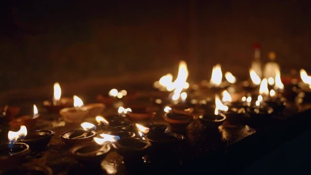 Oil lamps flicker in serene Buddhist temple, flame glow in dark, symbolize peace, faith. Devotees light votives, meditate, spiritual practice. Reflections dance on walls, tranquil ritual atmosphere.