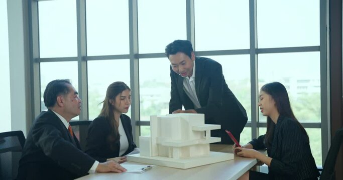 Asian businessman talking with team in meeting room. They dissing about building model and design together.