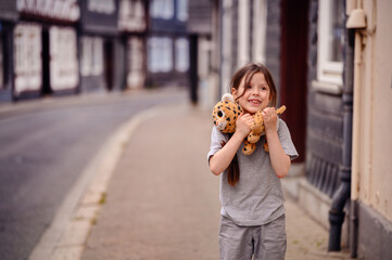 Smiling girl holding a plush toy on a quiet village street