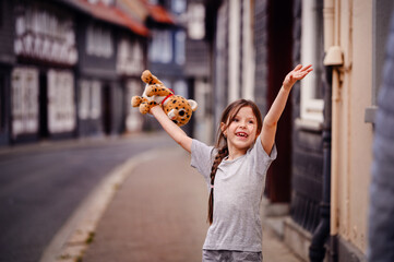 Joyful girl playing with a plush toy on a cobblestone street in a historic town