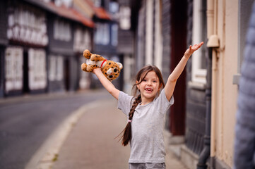 Joyful girl playing with a plush toy on a cobblestone street in a historic town