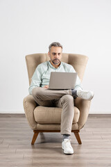 Freelancer concept. Man in armchair chilling and using his laptop. Remote job working from home.