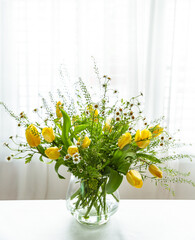 Bouquet of yellow tulips and daisies in a vase on the table