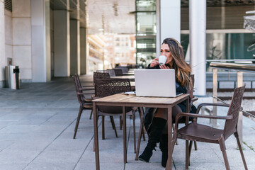Businesswoman drinking coffee on the terrace of a bar with her laptop