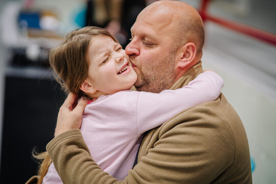 Valmiera, Latvia - February 17, 2024 -  a dad kissing a smiling young daughter on the cheek in an affectionate embrace.