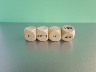 Turned a dice and changes the German expression du schaffst das nicht (you can not do it) to du schaffst das schon (you can do it). Beautiful blue background, grey table. Business concept. Copy space.