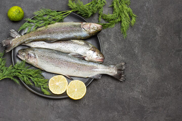 Raw fish trout with lemon wedges on black plate