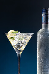 Vodka Cocktail in glass and ice-cold bottle close up on blue degraded background with copy space. Vertical format.