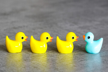 Miniature colorful toy ducklings on a gray background, 1 duck is not like everyone else, unique
