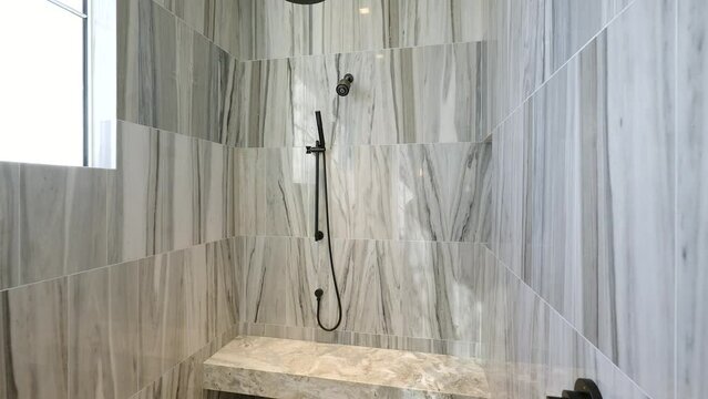 Contemporary bathroom design of walk in chrome shower with adjustable rail covered with grey melange tiles and bench seat lightened by window in side wall
