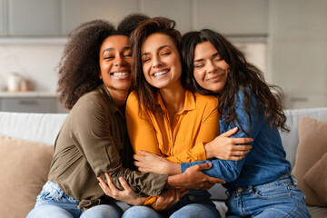 Three joyful young multiethnic women hugging and smiling together indoor - obrazy, fototapety, plakaty
