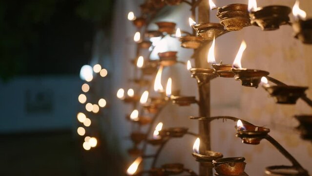 Rows of burning oil lamps at Buddhist temple in Vesak night. Peaceful flame lights reflect spiritual atmosphere, tradition, celebration. Devotees meditate, honor Buddha teachings with light.