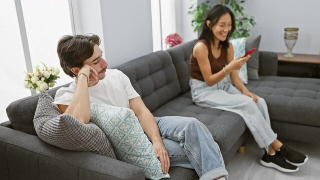 Interracial couple relaxes in a modern living room with a woman laughing at her phone and a contemplative man