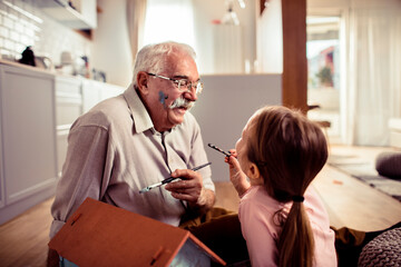 Grandfather and granddaughter painting a toy house together at home