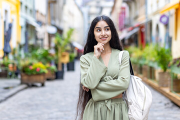 Indian young beautiful woman in a green suit with a backpack standing outside in the middle of the...