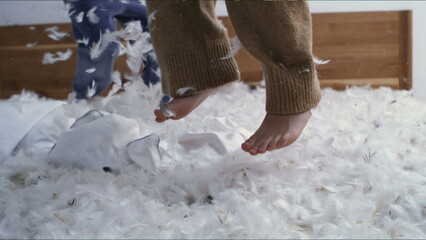 Closeup children feet bouncing in bed in the midst of feathers flying in the air in super slow motion. carefree childhood emotion of kid playing