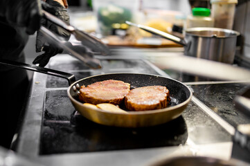 Professional chef cooking beef steak in frying pan on stove in restaurant kitchen