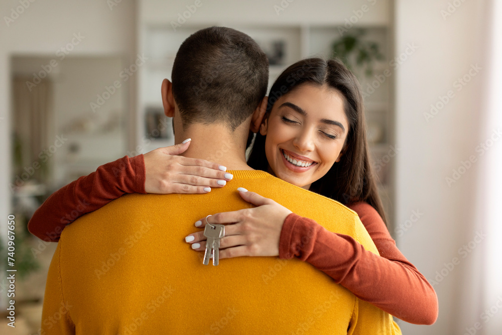 Sticker happy young woman hugging husband and holding home keys in hand