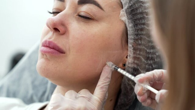 Beautician doctor makes botox injection in the cheekbone of young beautiful woman. Extreme close up 4k shot. Beauty technology concept