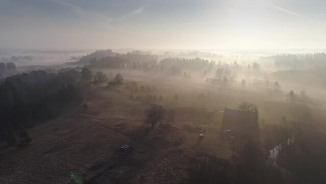 Aerial drone shot of foggy sunrise over rolling landscape countryside, house, forests and fields.