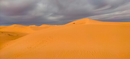 Fototapeta na wymiar A sweeping panorama captures the vast expanse of golden sand dunes stretching as far as the eye can see, forming an arid desert under a partly cloudy blue sky in Timimoun, Algeria.