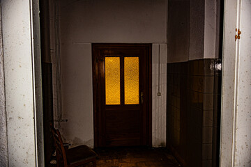 Alte Eingangstür in verlassenem Gebäude durch die gelblich bedrohliches Licht scheint