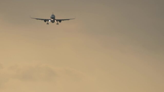 Footage of a jet plane approaching landing. Passenger airliner flies in the sunset sky, front view, long shot
