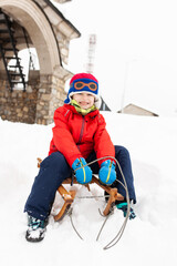 Fototapeta na wymiar Little boy sitting on an old wooden sledge on a cold winter day with snow.