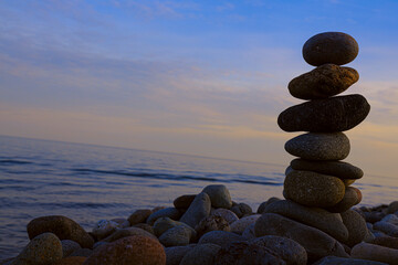 Balance pebble stone in the stoned beach at sunset. Stack of zen stones in harmony and balance with sea view. minimalist view of  stacked arrangement of pebbles on serene beach. mountain on background