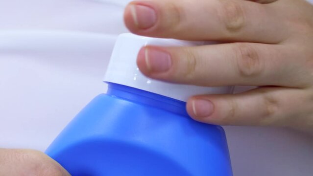 Female hands opening laundry detergent gel for washing machine with measure cup. Using fabric softener for laundry