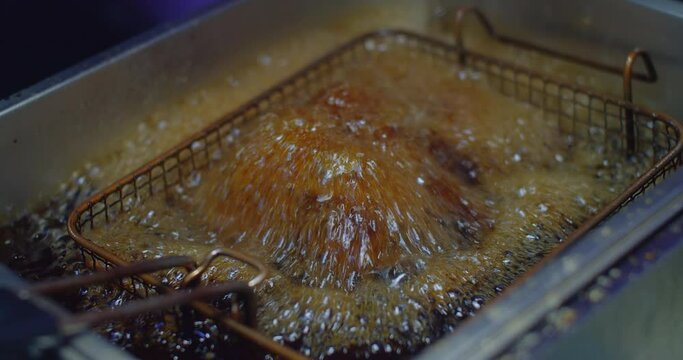 Close-up of chicken deep frying in oil, bubbles simmering in a stainless steel deep fryer