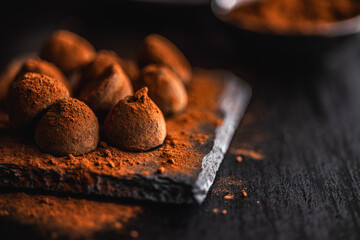 Chocolate truffles covered with cocoa powder on black table.