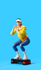 Sporty young woman with stepper doing aerobics on blue background