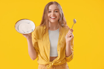 Beautiful young woman with empty plate and spoon on yellow background