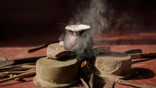 Sri Lankan housewife performs traditional milk boiling ritual over open fire for Vesak. White froth overflows pot, symbolizing prosperity, during full moon Poya day as homage to Buddha.