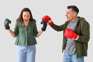 Young couple in boxing gloves quarreling on light background