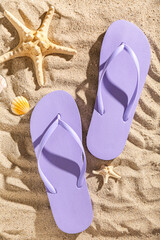 Fototapeta na wymiar Pair of purple flip flops with starfishes on sandy background