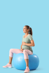 Sporty pregnant woman with fitball training on blue background