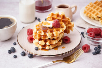 Plate of tasty waffles with berries and maple syrup on white background