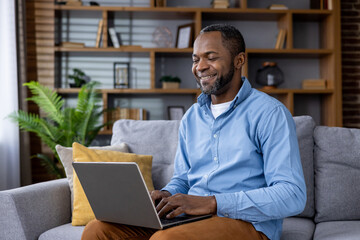 Smiling african american man using laptop at home on comfortable sofa