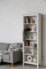 Modern shelf unit and grey sofa near white brick wall