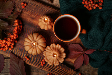 Beautiful autumn composition with burning candles in shape of pumpkin and mug of tea on wooden background