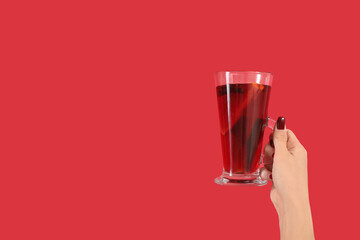 Female hand with glass cup of warm mulled wine on red background