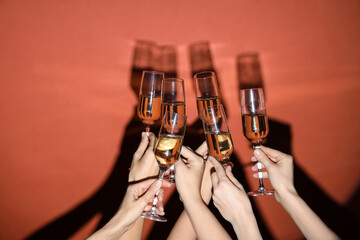 Female hands with glasses of champagne on orange background